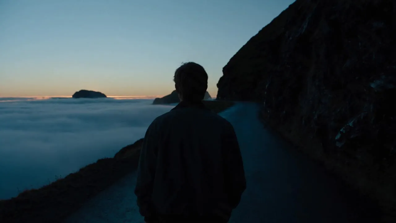 A silhouette on a mountain road above a sea of clouds at twilight